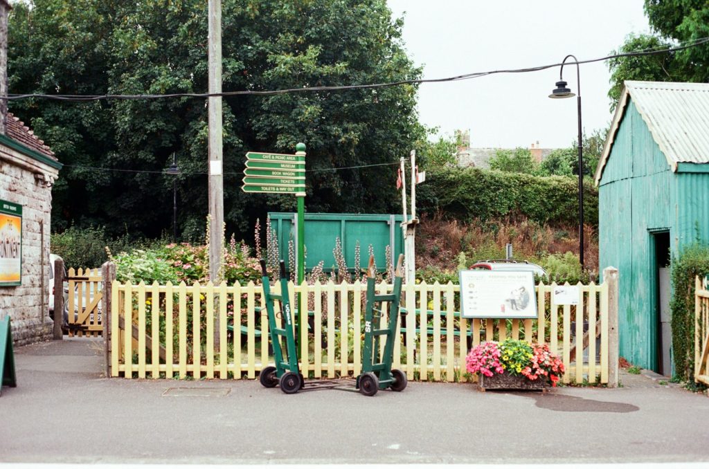 Green railway signals stand beside a wooden fence.
